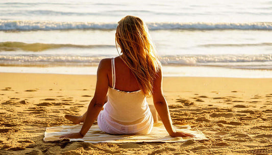 Woman relaxing on a sand-free towel at the beach, enjoying the calm ocean waves.