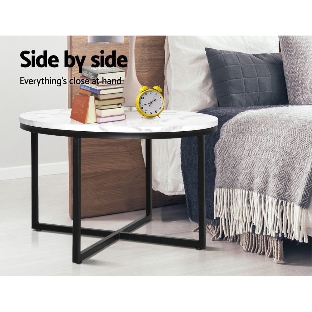 Modern round coffee table with marble effect top beside a cozy bed, perfect for stylish living room decor.