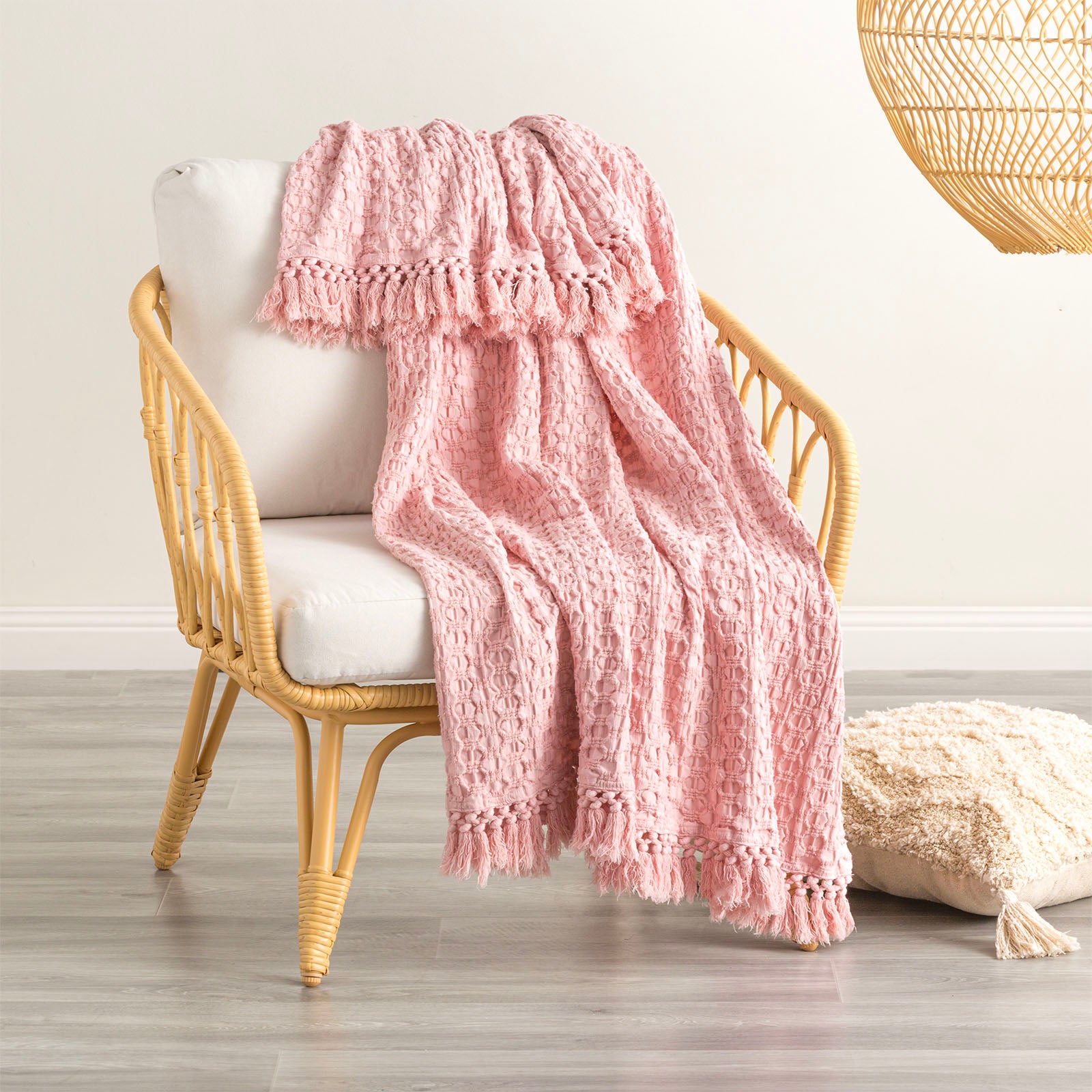 Blush Alysian washed cotton textured throw blanket draped over a stylish chair, perfect for cozying up any living space.