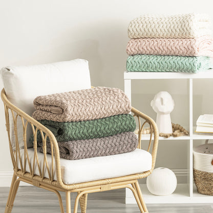 Lenni 100% Cotton Knitted Vapour Throws in neutral tones stacked on a chair and shelf, showcasing chunky knit texture.