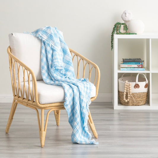 Light blue cotton throw blanket draped over a rattan chair in a cozy living space, showcasing vintage washed texture and style.