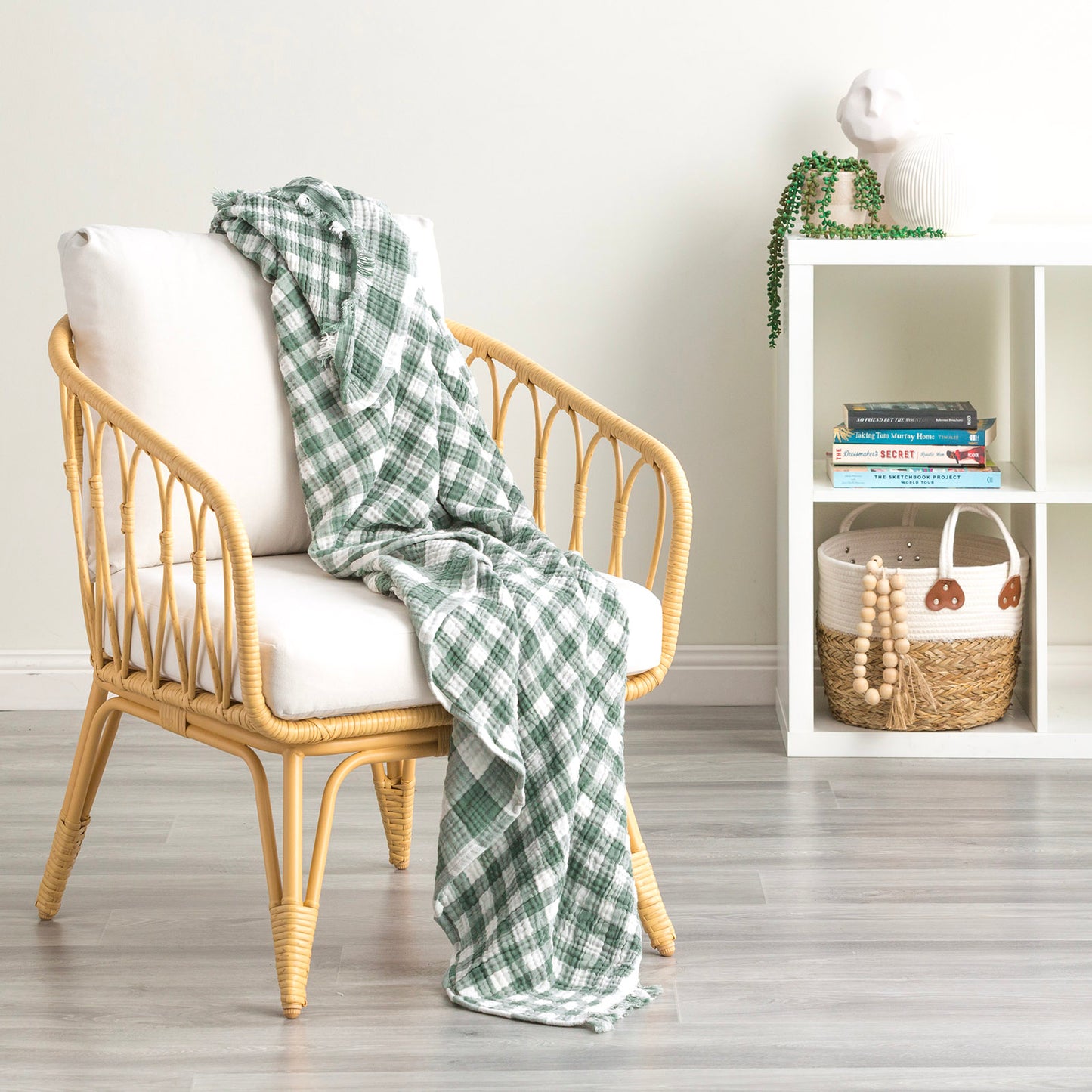 Cozy green plaid cotton throw blanket draped over a stylish rattan chair in a modern living room setting.