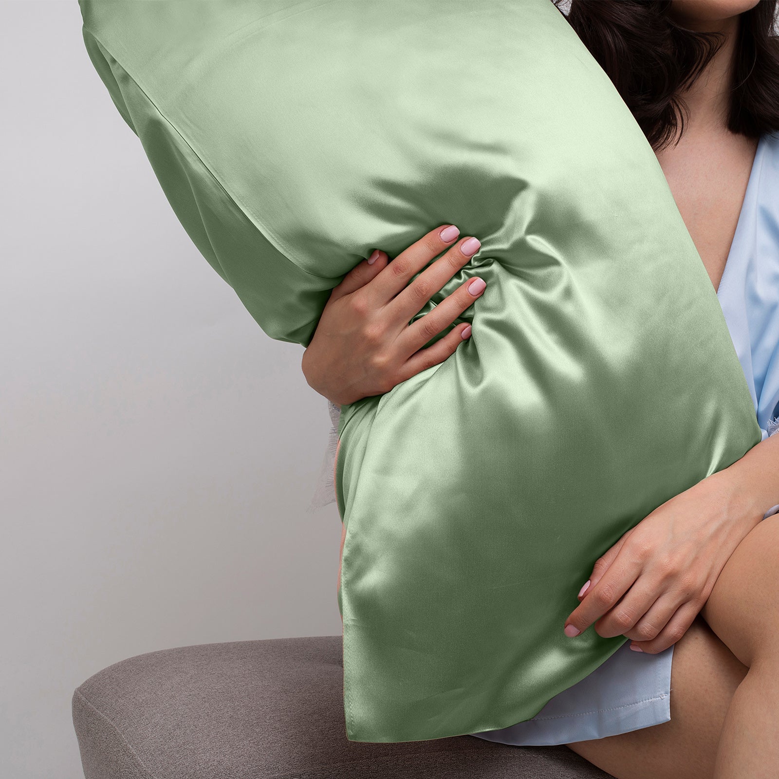 Elegant sage green satin pillowcase held against a soft background, showcasing luxury bedding comfort and style.