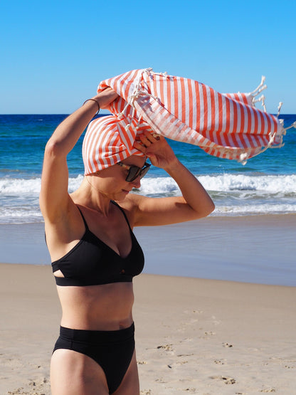 Woman wearing a striped towel on the beach, enjoying the sun and ocean waves. Perfect for beach days with style.