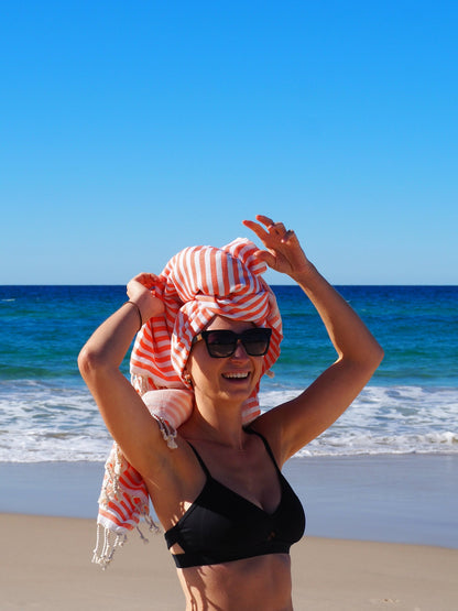 Woman wearing a coral striped beach towel on the beach, enjoying the sun and waves on a beautiful day.