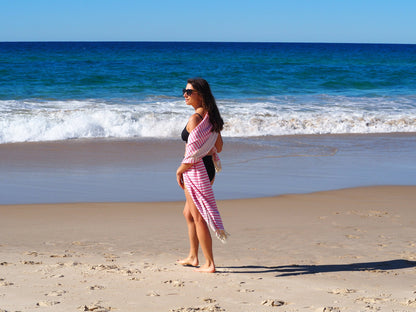 Woman in a stylish beach outfit with a towel on the beach, enjoying a sunny day by the water.