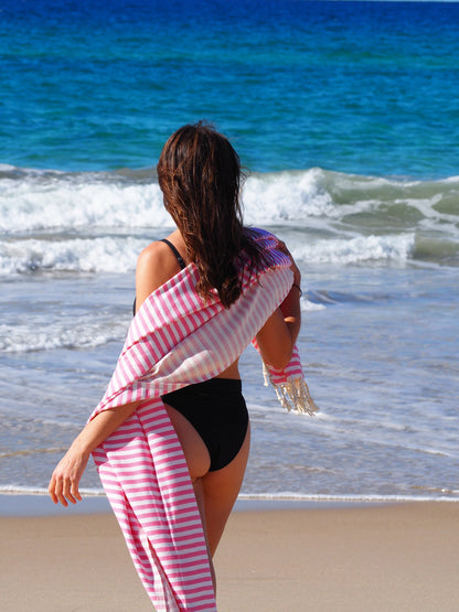 Woman draped in Portsea Turkish cotton beach towel on the beach, enjoying a sunny day by the ocean.