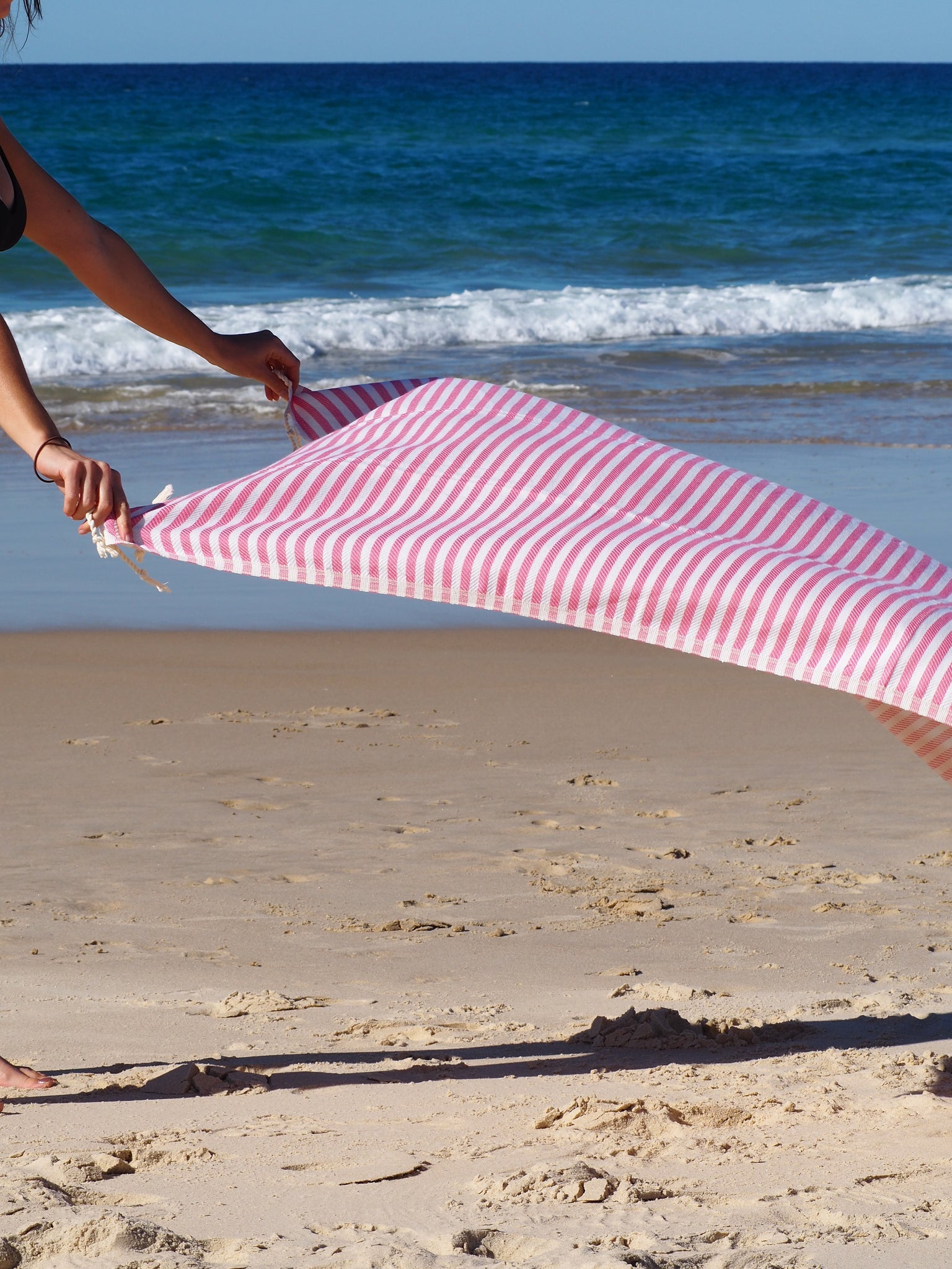 Woman holding Portsea Turkish cotton beach towel in rose on sandy beach, ideal for quick drying and stylish relaxation.