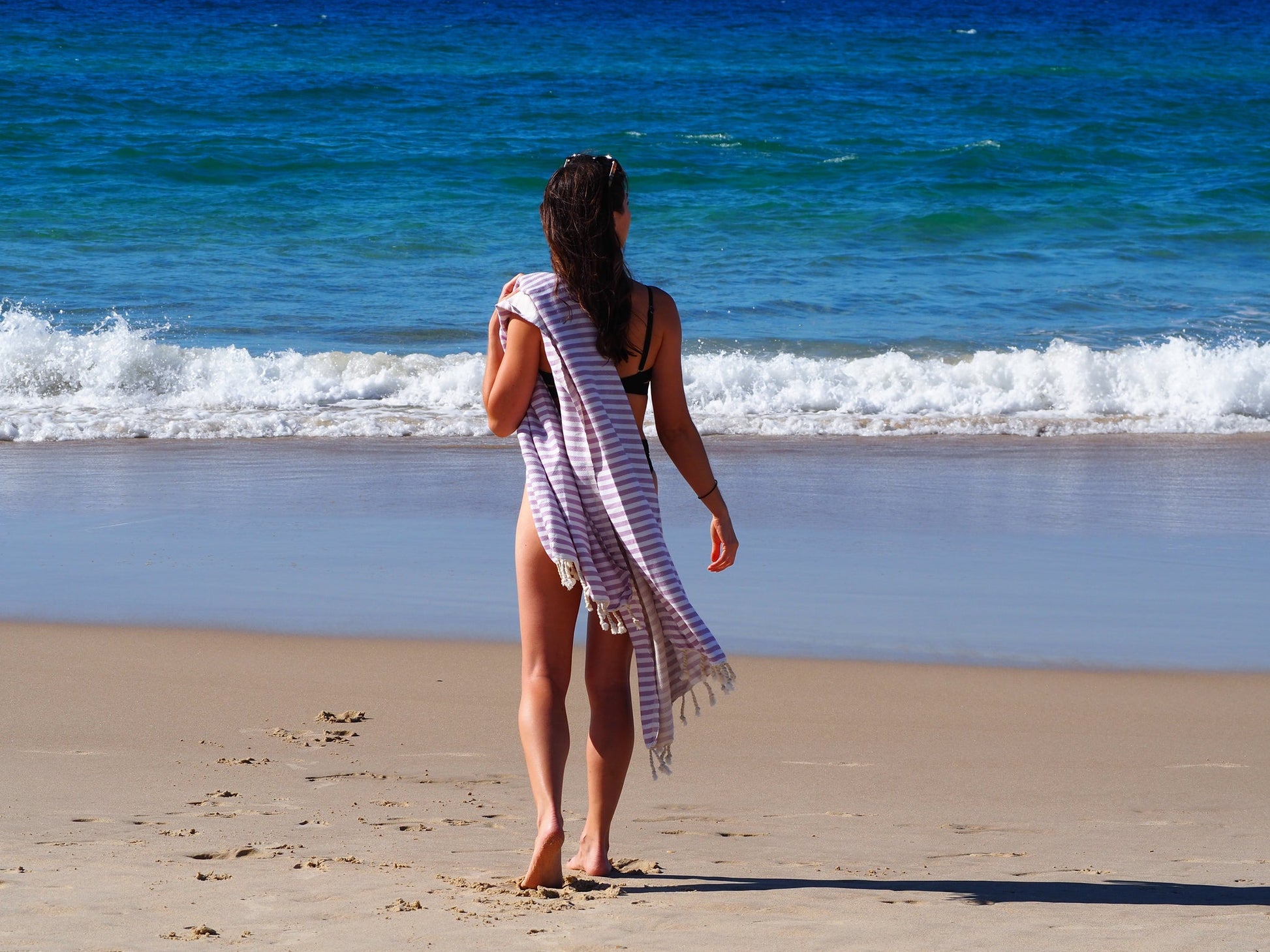 Woman on beach holding a lilac Turkish cotton beach towel, ready to enjoy a sunny day by the sea.