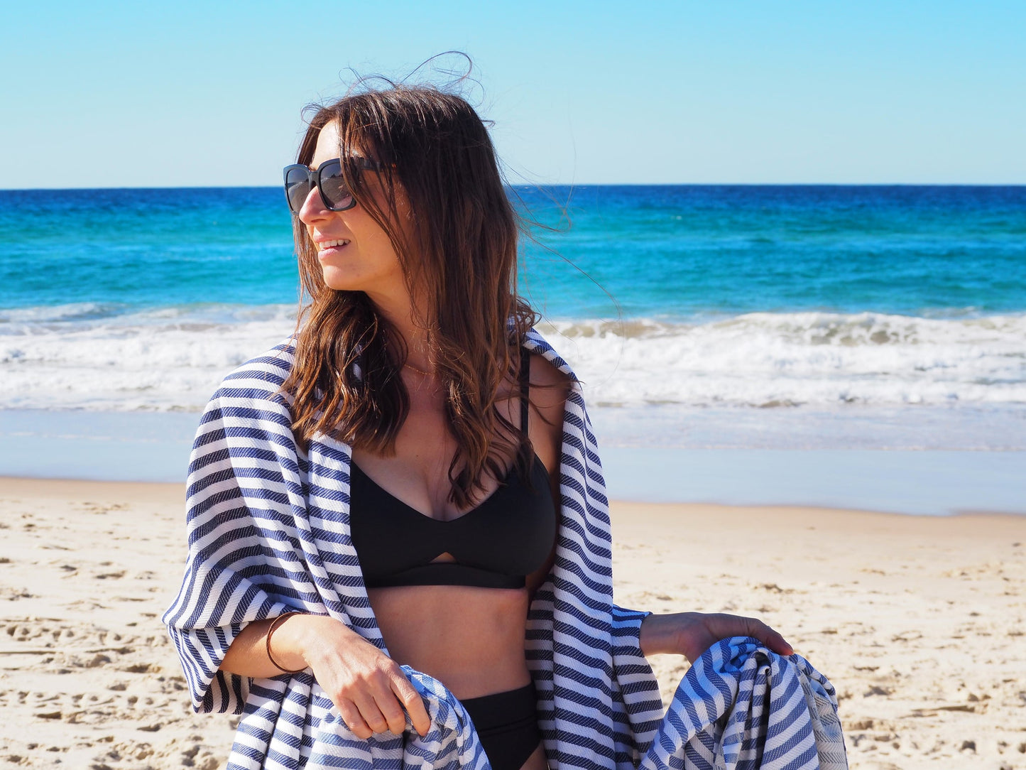 Woman in sunglasses enjoying the beach wrapped in a stylish striped towel, perfect for a sunny day by the sea.