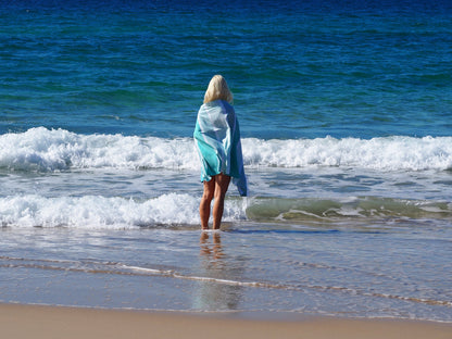 Woman on beach wearing a Turkish cotton beach towel, enjoying the ocean waves and sunny weather.