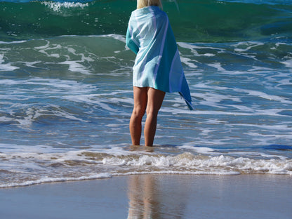 Woman in ocean waves wearing Portsea Turkish cotton beach towel in ocean color, enjoying a sunny beach day.