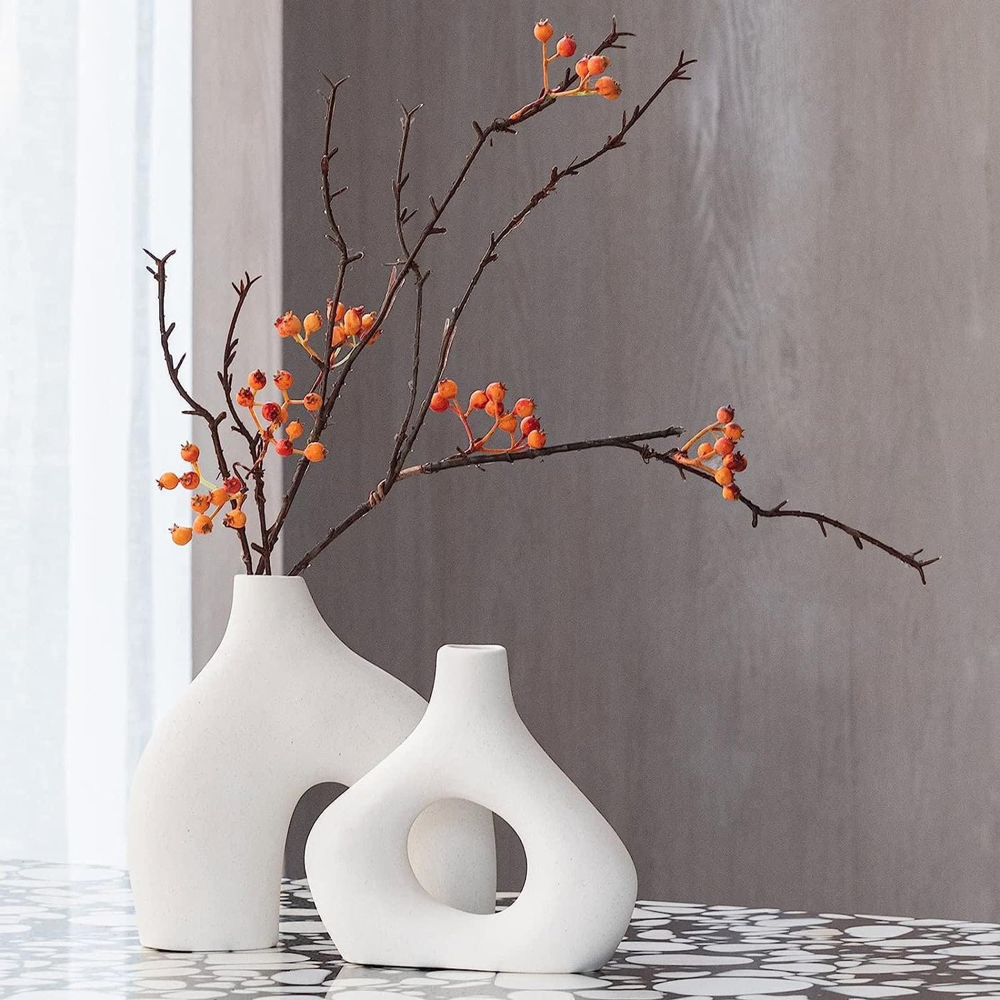 Modern white ceramic vases with branches and berries, perfect for stylish home decor and floral arrangements.