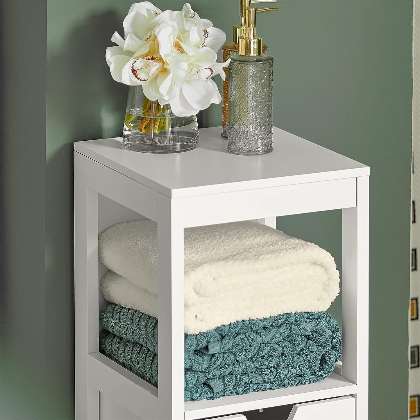 Stylish white freestanding cabinet with towels, flowers, and soap dispenser for organized storage.