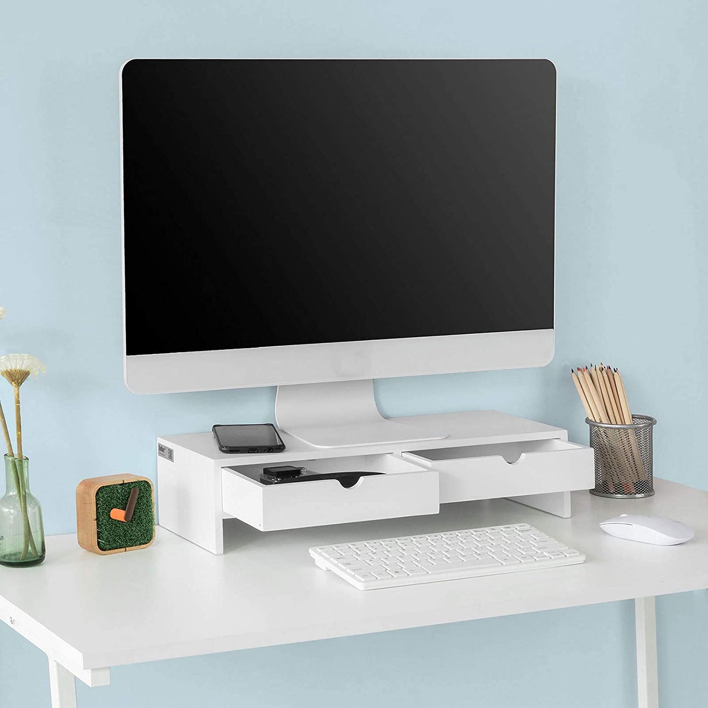 White monitor stand desk organizer with two drawers elevating the monitor and providing storage for gadgets and a keyboard.