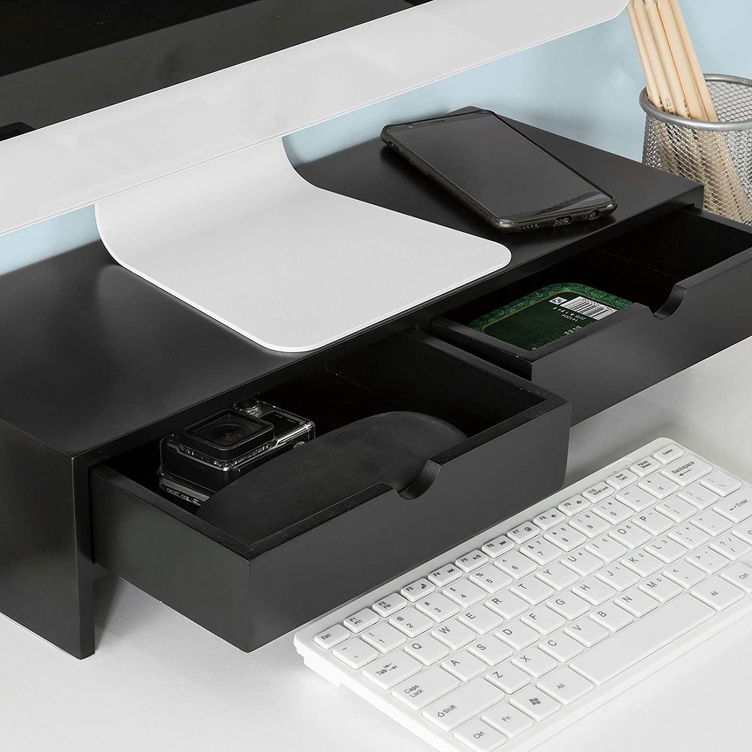 Black monitor stand desk organizer with two drawers, keyboard, and gadgets on a stylish workspace.