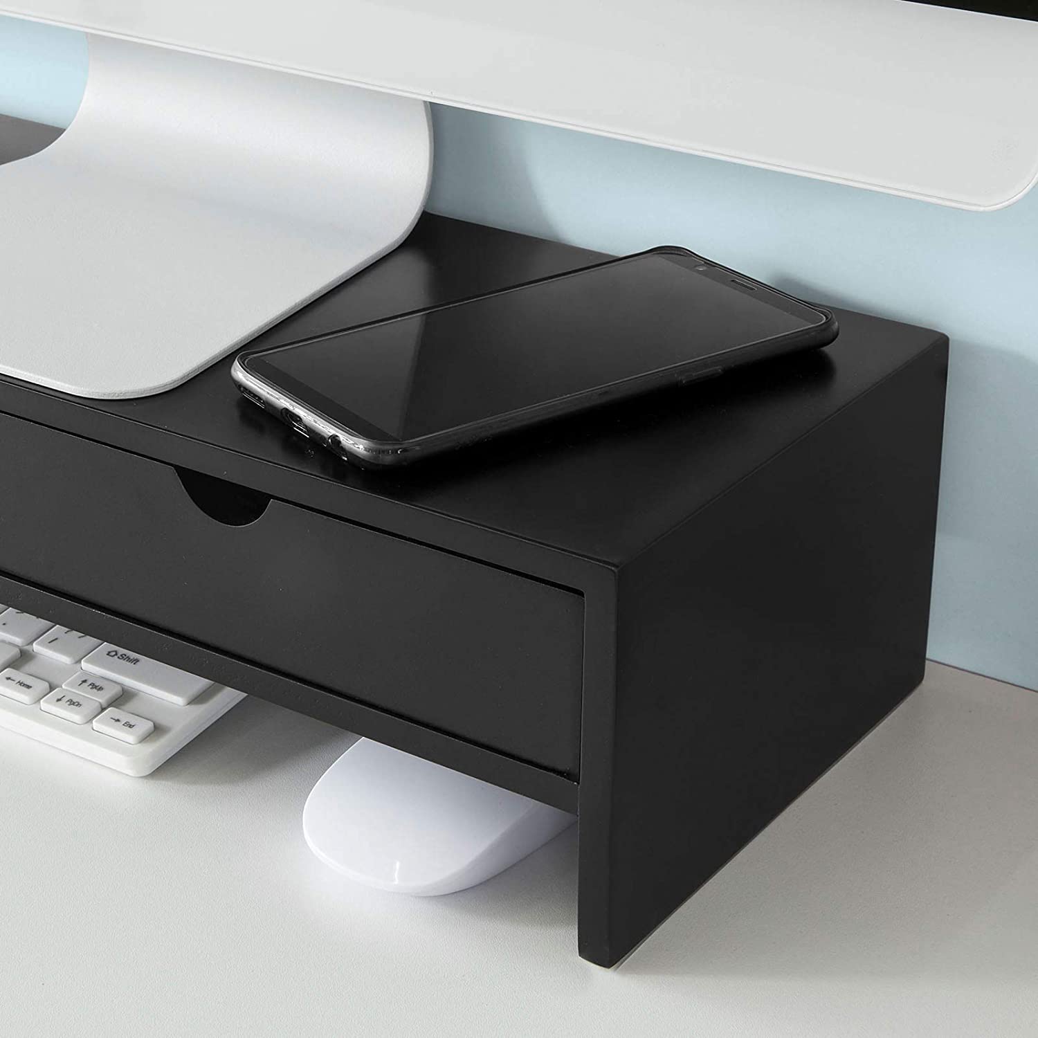 Black monitor stand desk organizer with drawer, smartphone, and keyboard, enhancing workspace efficiency and comfort.