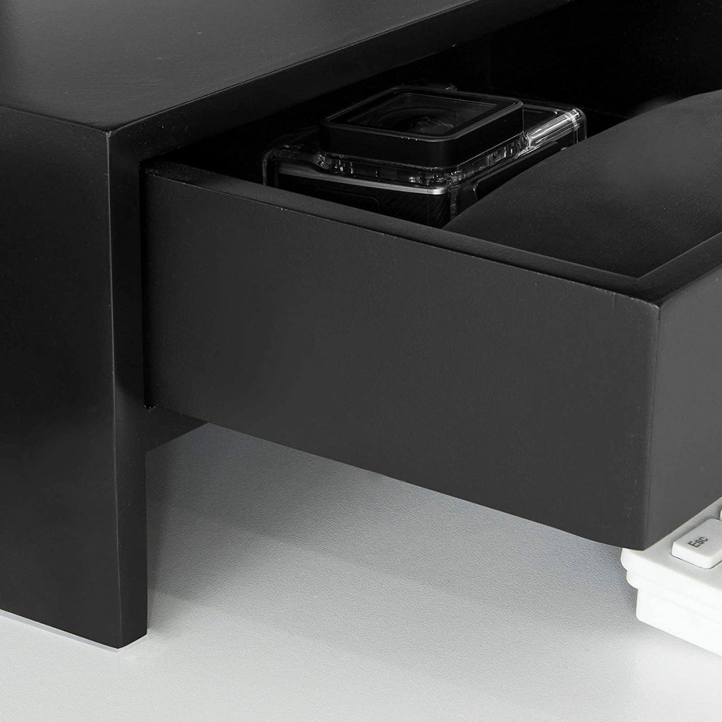 Black monitor stand desk organizer showing a drawer partially open with storage space for gadgets.