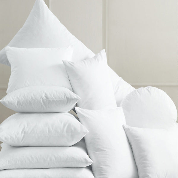 Assorted white polyester cushion inserts in various shapes and sizes stacked creatively for a cozy home decor display.