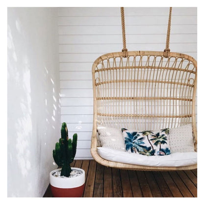 Cozy hanging chair with palm tree cushion, cactus plant, and wooden deck for a tropical home vibe.