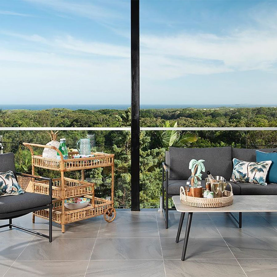 Modern outdoor living space with sofa, stylish cushion covers, and a scenic view of lush greenery and ocean.