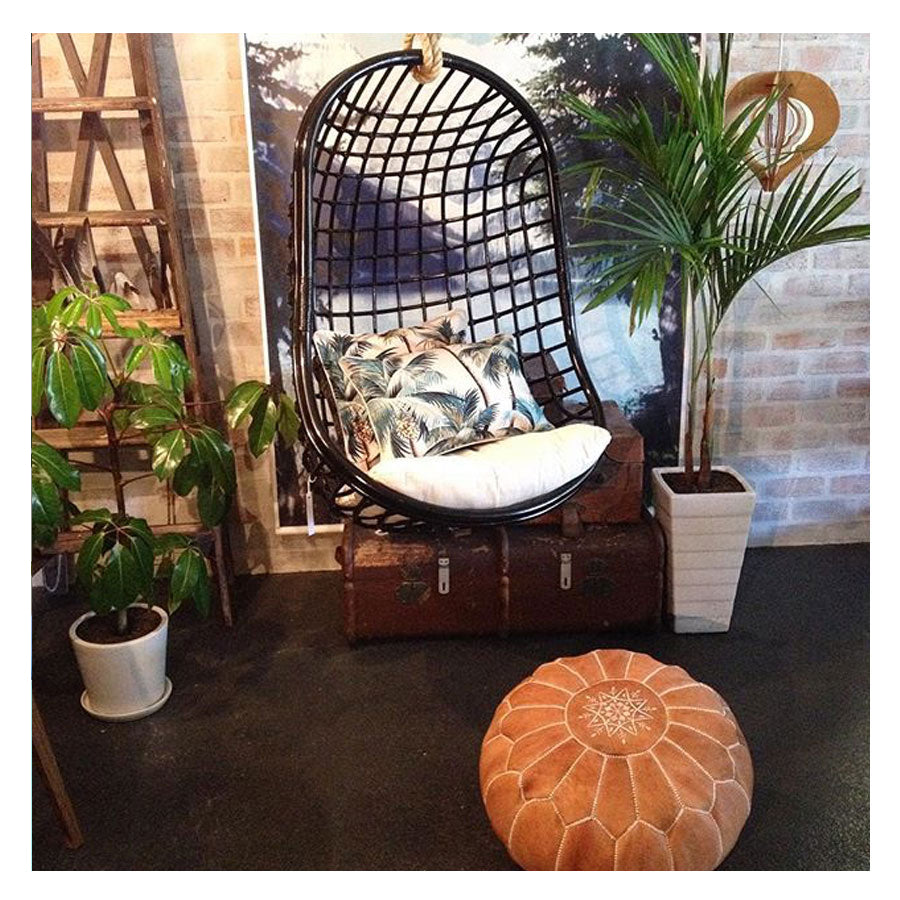 Cozy hanging chair with tropical cushions, surrounded by plants, evoking a relaxing indoor oasis.