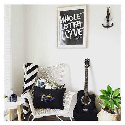 Cozy living space with palm tree cushion cover, acoustic guitar, and modern wall art, perfect for tropical home decor.