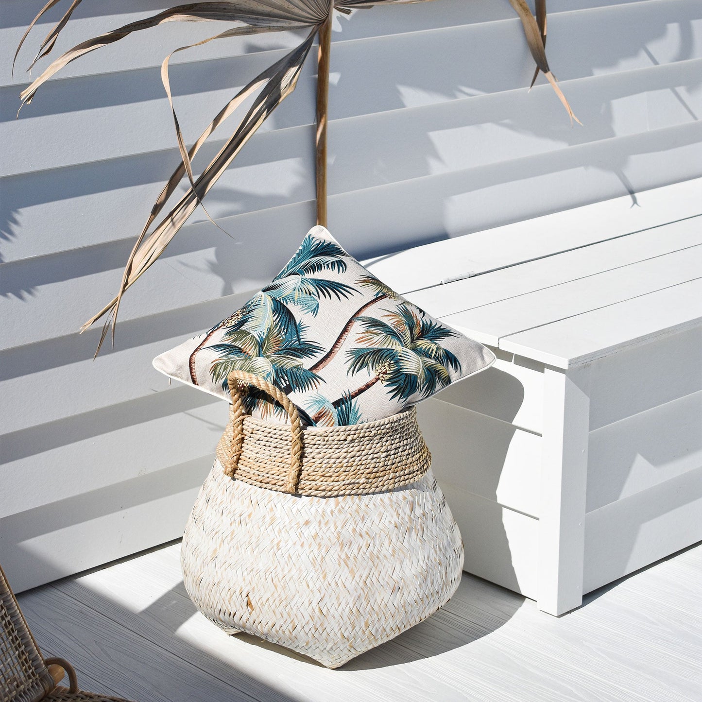 Cushion cover with palm trees design resting on a woven basket in a tropical setting, perfect for indoor or outdoor decor.