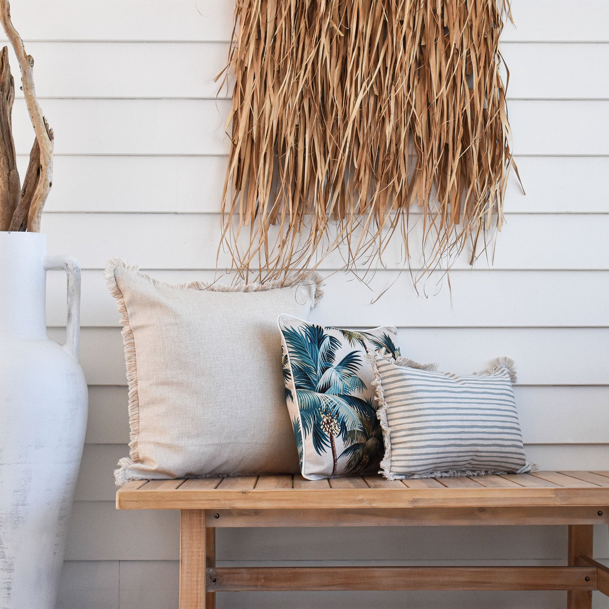 Tropical cushion covers on a wooden bench, featuring palm prints and textured fabrics for a stylish home decor.