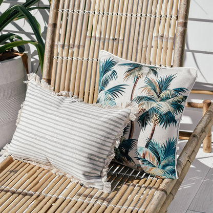 Two decorative cushion covers on a bamboo chair, featuring palm trees and striped designs for a tropical home vibe.