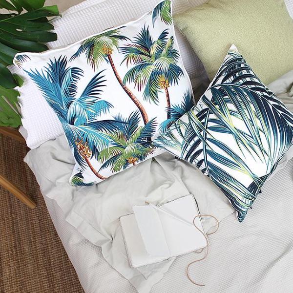 Decorative cushion covers with palm tree prints on a cozy bed setting, perfect for a tropical home decor.