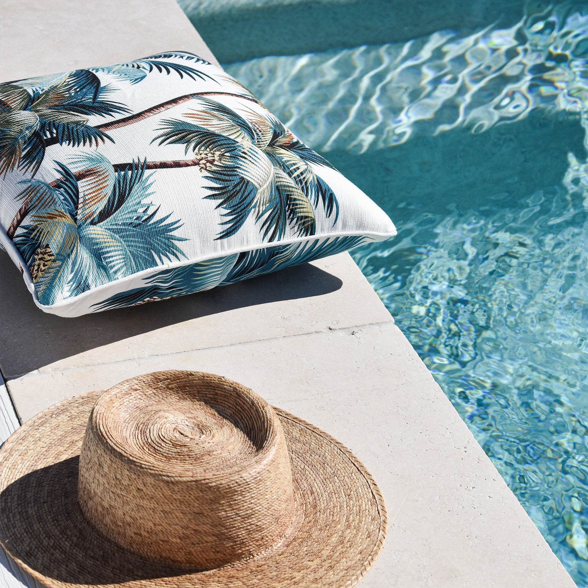 Tropical palm tree cushion cover by the poolside, perfect for indoor or outdoor decor with water-resistant fabric.