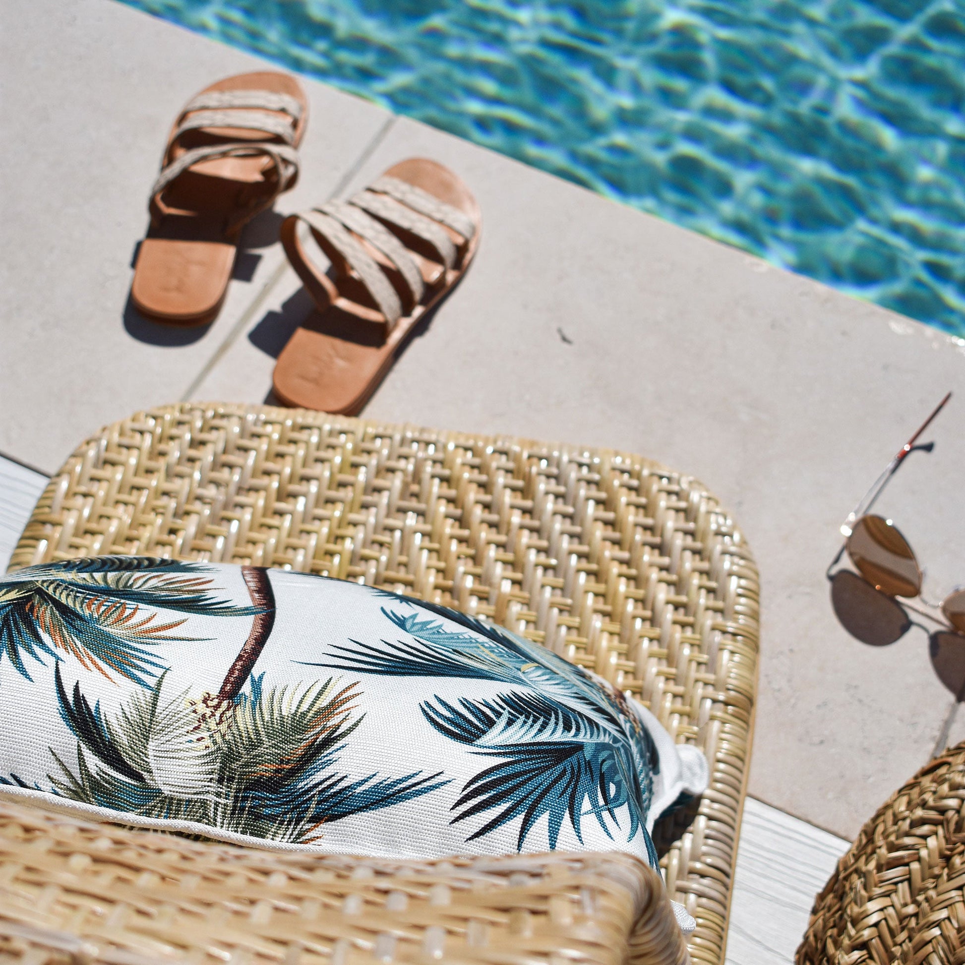 Cushion cover with palm trees placed on a woven chair beside a pool, perfect for tropical outdoor decor.