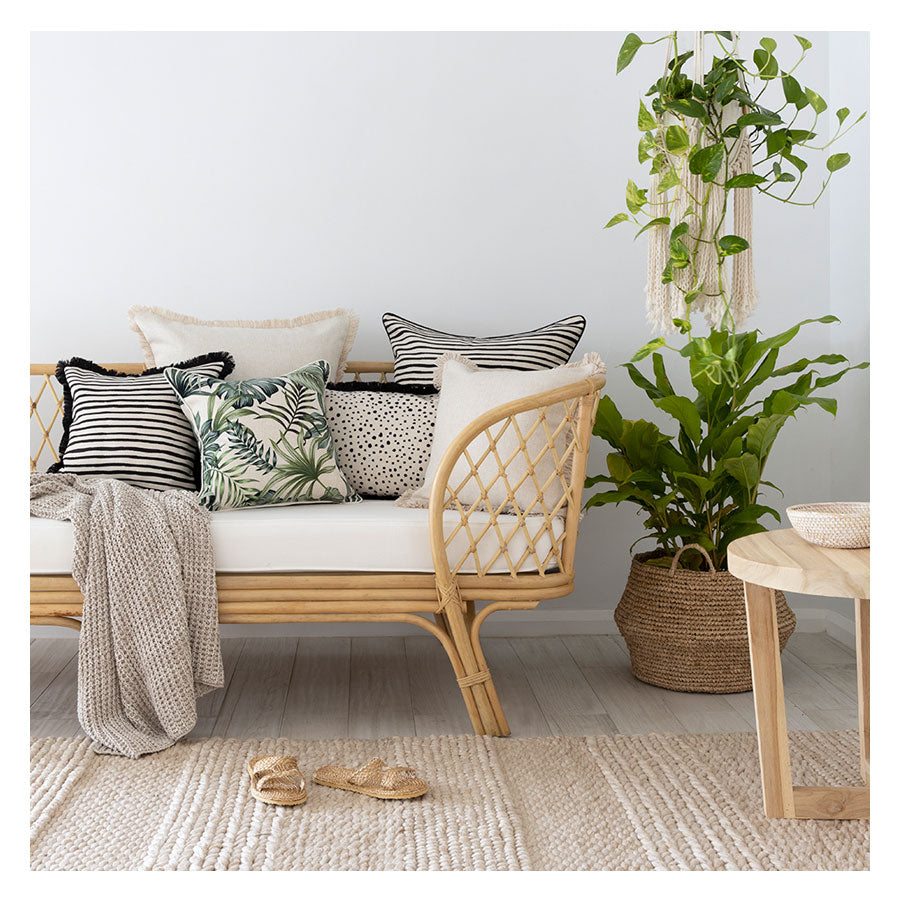 Stylish sofa with tropical cushion covers, plants, and a cozy atmosphere, perfect for indoor or outdoor living.