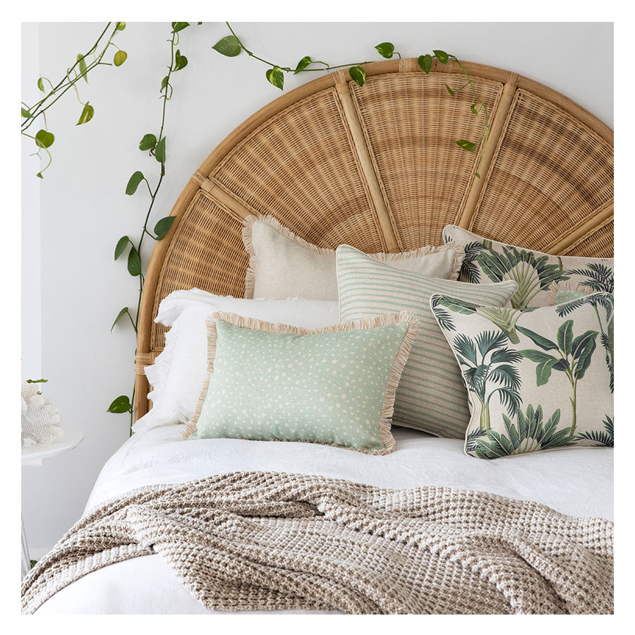 Decorative cushion covers on a bed with a rattan headboard, featuring tropical prints and soft textures for a stylish home decor.