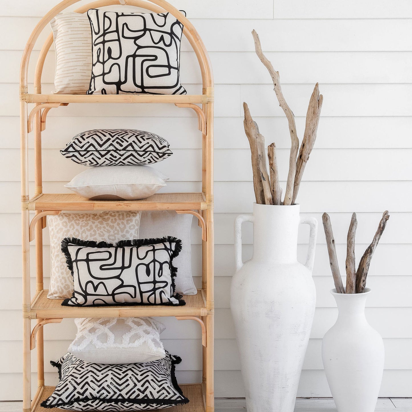 Stylish display of black and white cushion covers on a wooden shelf with decorative vases and branches.