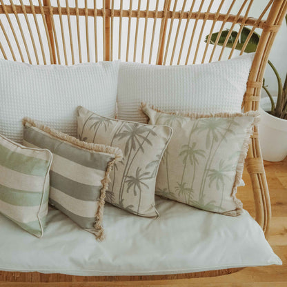 Luxurious cushion covers with palm prints and stripes on a cozy rattan sofa, enhancing tropical decor.