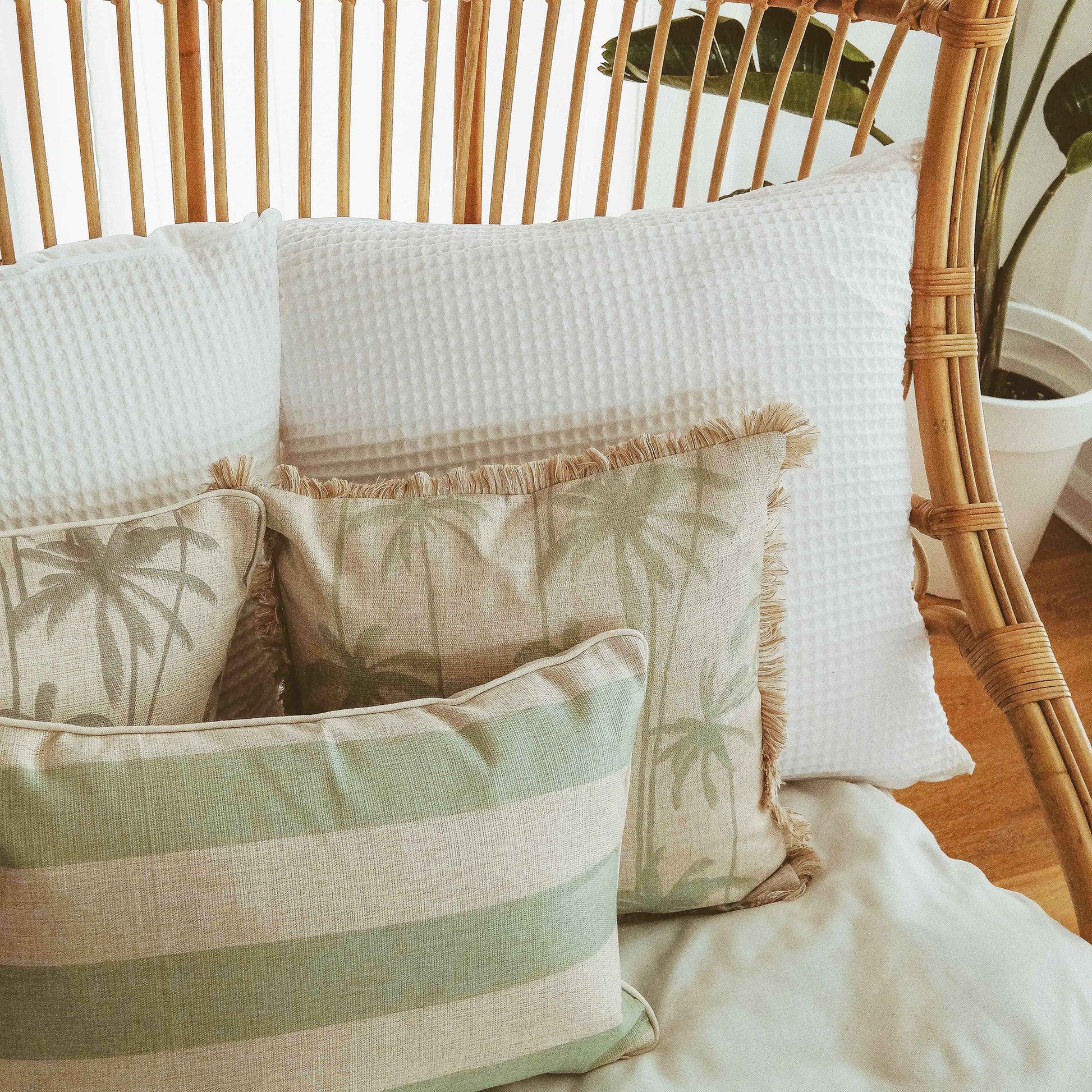 Decorative cushion covers with palm prints and textures, arranged on a cozy chair in a tropical-inspired home setting.