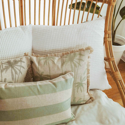 Decorative cushion covers with palm prints and textures, arranged on a cozy chair in a tropical-inspired home setting.