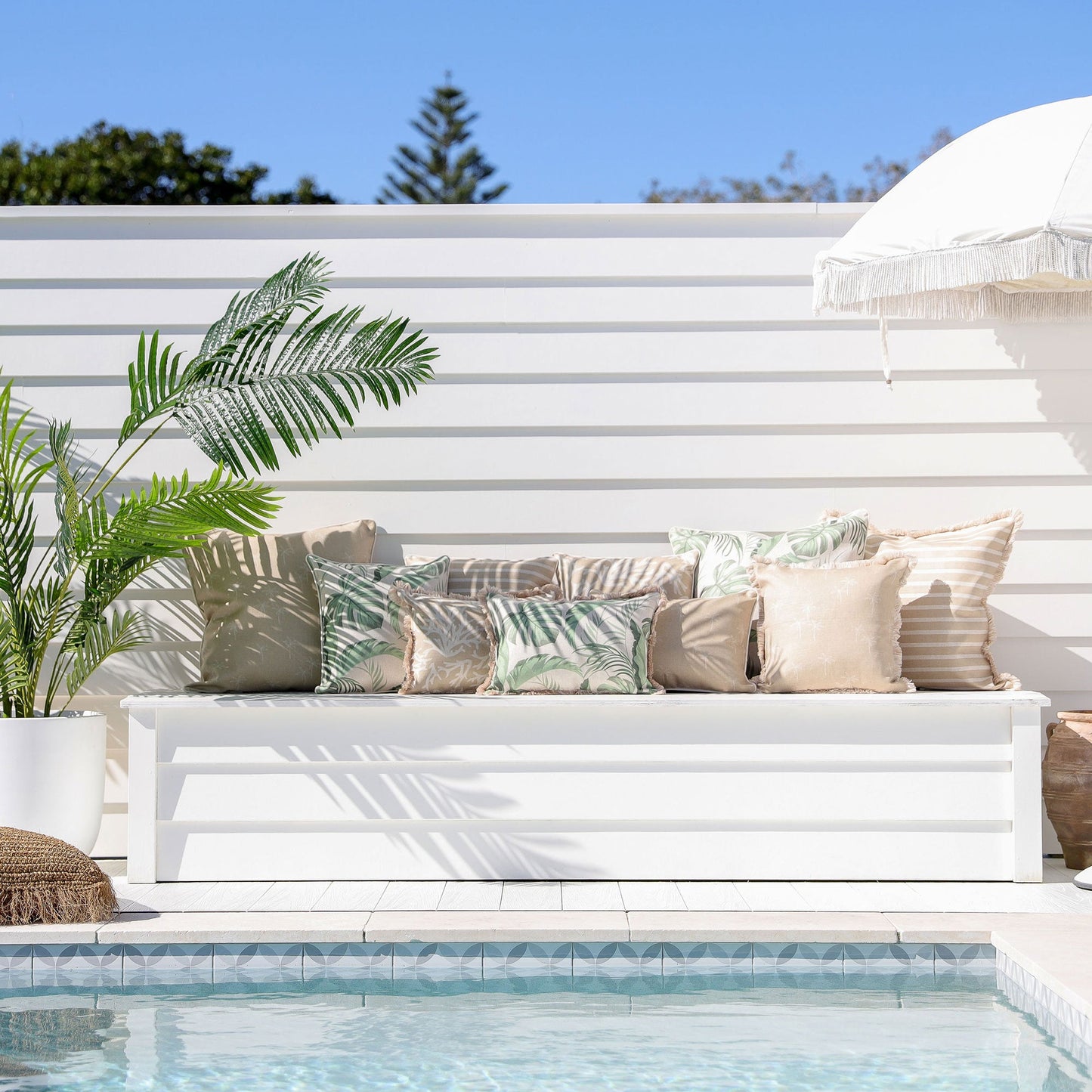 Stylish outdoor seating with cushion covers, tropical decor, and palm leaves near a pool, creating a luxurious ambiance.