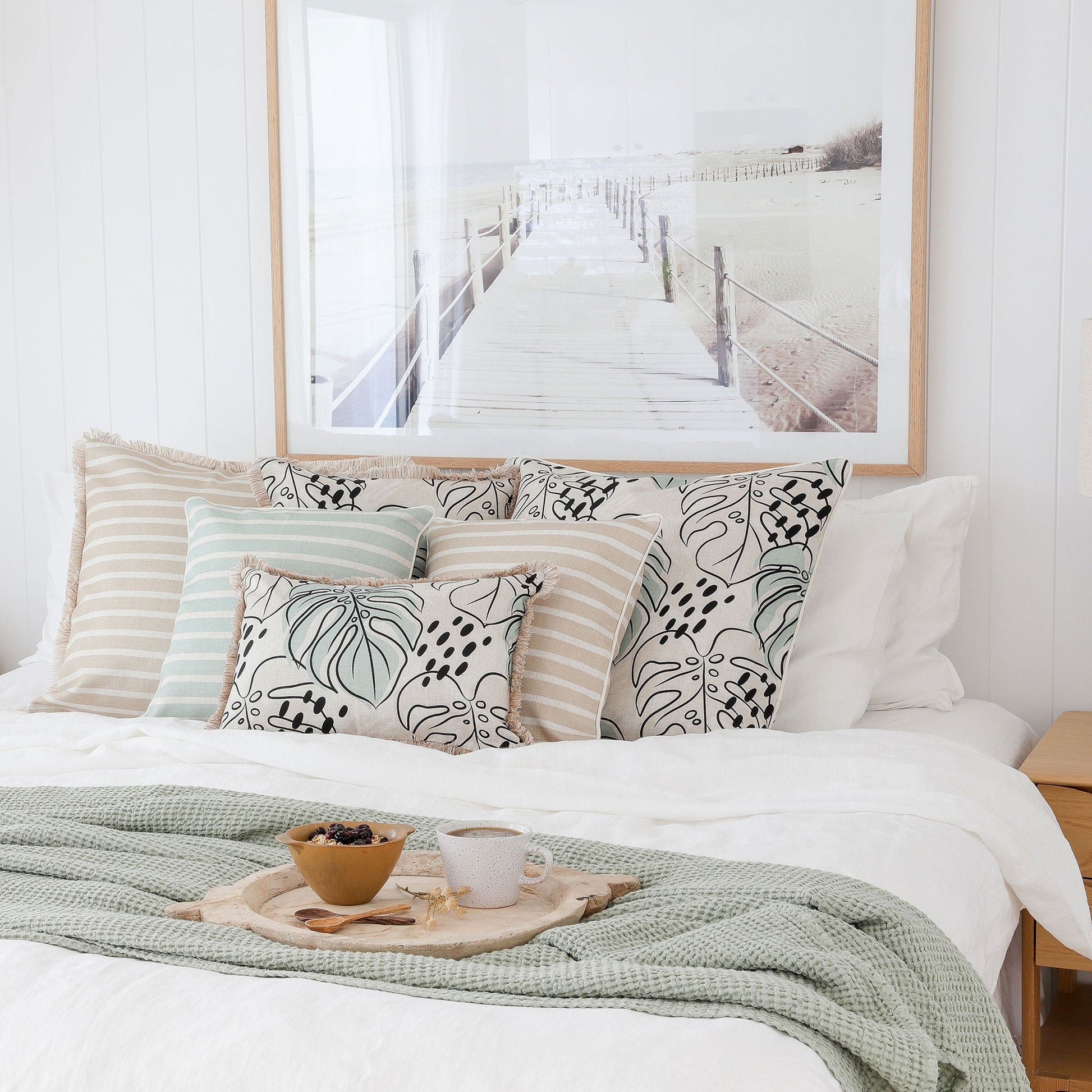 Cozy bedroom scene featuring stylish cushion covers on a bed with a beach-themed backdrop and decorative accessories.