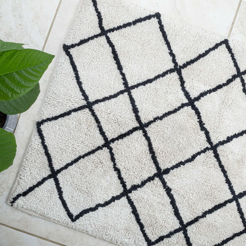 Soft cotton bath mat with a tufted jacquard design in cream and black, ideal for stylish bathroom placement.