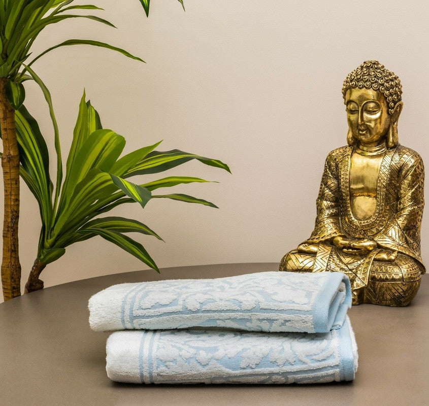 Premium cotton bath towels in jacquard white and blue design, styled with a Buddha statue and green plant for a serene bathroom ambiance.