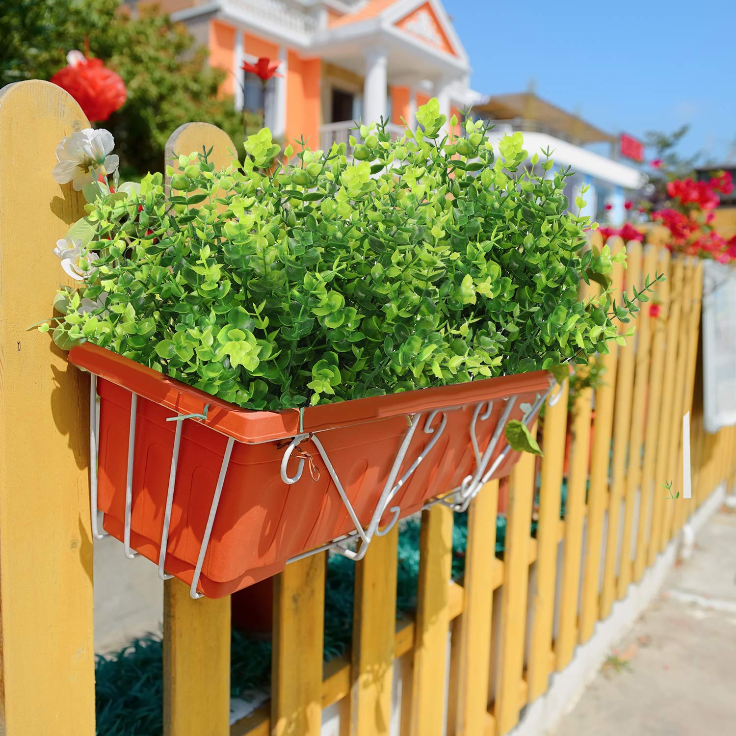 Bright faux eucalyptus plants in an orange planter on a fence, perfect for home and garden decor.