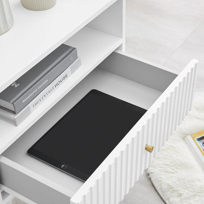 White Lucia bedside table with open drawer showing books and a tablet, featuring fluted design and satin finish.