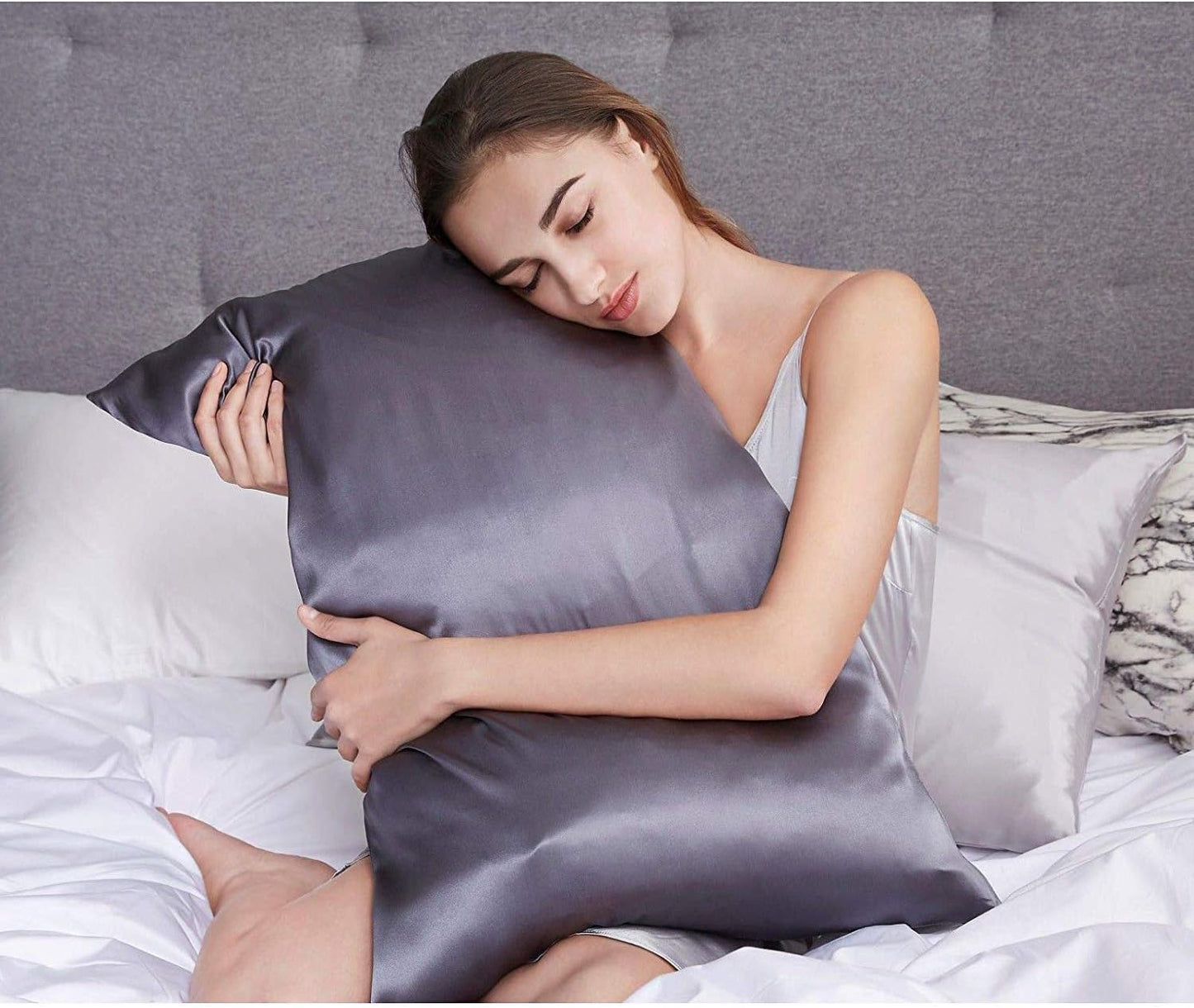 Woman embracing luxury mulberry silk pillowcase in charcoal color for a comfortable sleep experience.