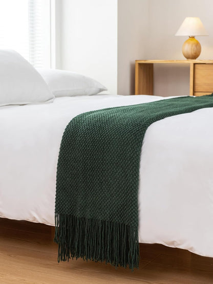 Forest green throw blanket draped over a bed, showcasing a modern knitted design with fringe detail for added elegance.