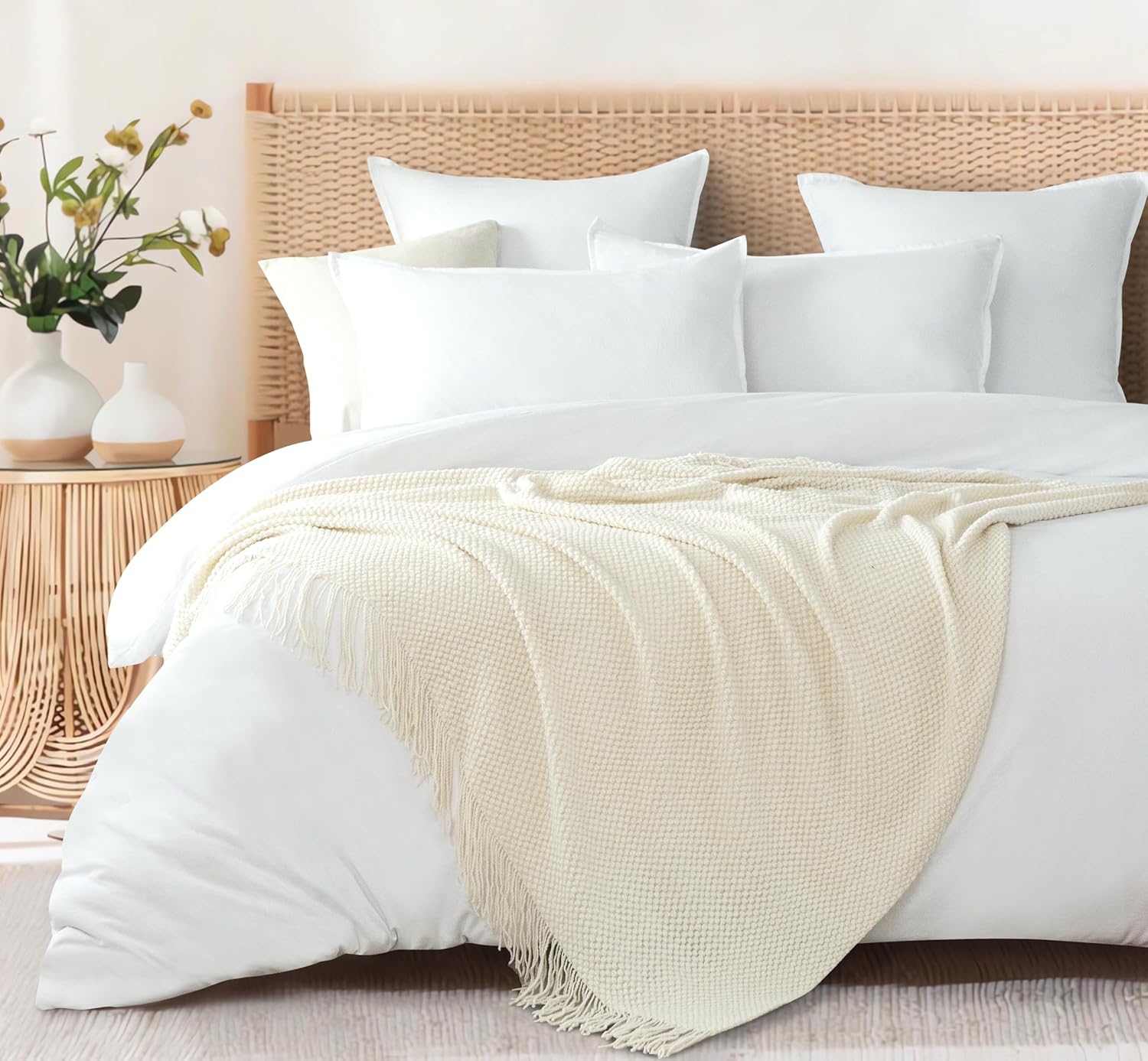 Cream throw blanket elegantly draped over a white bed with pillows, enhancing a cozy and modern bedroom setting.