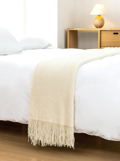 Cream-colored micro plush knitted woven throw blanket draped over a bed, adding cozy elegance to the room decor.