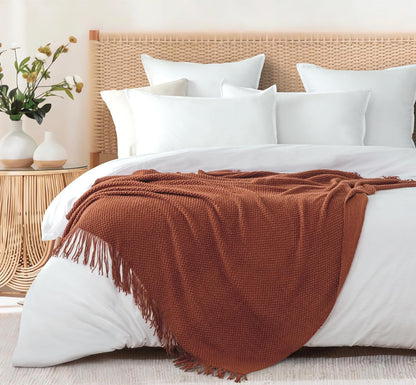 Terracotta micro plush knitted woven throw blanket on a bed, adding warmth and elegance to home decor. Perfect for couches or sofas.